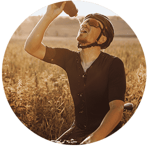 Radfahrer trinkt Wasser aus einer Flasche, um sich während des Sports zu erfrischen, umgeben von Natur.
