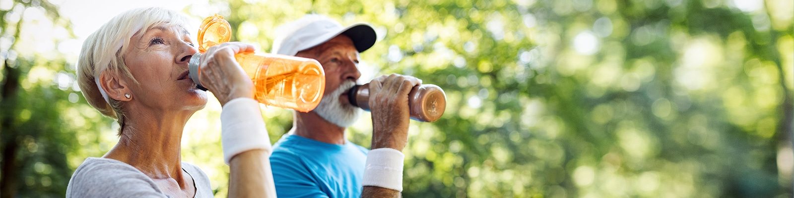 Aktive ältere Paare trinken Sportgetränke im Freien, ideal für Hydration beim Sport.